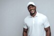 © Yuliia - Happy African American man in white polo shirt and cap smiling at camera against gray background for lifestyle and fashion content.