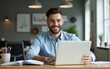 © Lucy - A smiling young man businessman sits in the office at the table and works on a laptop. High quality