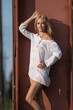 © shymar27 - Young woman with long blonde hair wearing a white blouse poses confidently against a rust-colored structure, showcasing a relaxed summer vibe and natural beauty