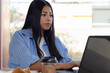 © Rangel - Young Mexican woman focused on her laptop screen, working efficiently from home or a remote location, with a cup of coffee and a croissant near the table.