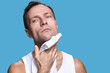 © DragonImages - Portrait of middle aged Caucasian man looking into camera while wiping neck with towel, showing clean shaven face and short hair against plain blue background