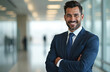 © miss irine - Attractive latino businessman smiles confidently in a modern office setting. He wears a blue suit, white shirt and tie. The background is blurred showcasing corporate facilities.