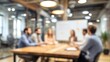 © Volodymyr - Blurred background of conference room meeting with a table surrounded by people sitting on orange chairs and stylish bokeh lamps overhead