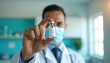 © miss irine - Doctor holds vial with vaccine wearing face mask. Medical professional shows liquid medicine for injection. Healthcare expert promotes immunization for global health.