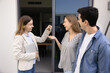© fizkes - Smiling real estate agent hands over keys to cheerful young couple standing outside their new home. First-time homeownership, success of property deal, positive relationship between client and agent