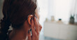 © SnapK/peopleimages.com - Hand, woman and touch hearing aid at house with ear device, testing sound and auditory assistance. Back, medical equipment and female person with disability, deaf and audio implant to improve speech
