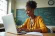 © Vadym - Young African American teacher works on laptop in classroom. Smiling woman prepares lesson online using computer and internet. Female instructor teaches virtually from school.