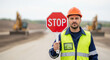 © Xenia - Construction worker holding a red stop sign on a road site. Male builder in safety vest and hard hat warning traffic. Roadwork and industrial safety concept