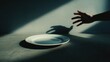 © pixelliebe - human shadow reaching toward an empty white plate on dark surface, representing hunger, eating disorder or diet