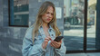 © Krakenimages.com - Woman in denim jacket frowns while tapping smartphone with finger on urban street; frustration confusion.