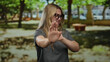 © Krakenimages.com - Woman with blonde hair expressing disgust with hands raised outdoors in a sunny park wearing glasses.
