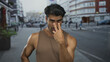 © Krakenimages.com - Young hispanic man in brown tank top shows finger to eyes for watching gesture on street; intimidation.
