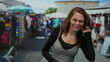 © Krakenimages.com - Young woman listening in an outdoor market, city setting, surrounded by bustling shops and vibrant street activity.