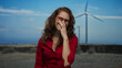 © Krakenimages.com - Woman smiling outdoors with long curly hair wearing red shirt and glasses in a field with windmill against blue sky