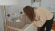 © Krakenimages.com - Woman bending over crib in cozy bedroom with soft lighting, mobile toys hanging above, creating a serene nursery ambiance inside a modern home