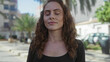 © Krakenimages.com - Woman smiling with eyes closed standing on a city street surrounded by tall buildings and greenery under a clear blue sky.