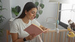 © Krakenimages.com - Young woman reading a pink book while sitting by a wooden cradle in a building nursery, turning pages and speaking softly; serenity.