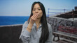 © Krakenimages.com - Young chinese woman smiling at the seaside promenade in an outdoor setting with the blue ocean as a backdrop on a sunny day.