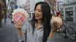 © Krakenimages.com - Young chinese woman holding yuan banknotes and a piggy bank outdoors on a bustling street
