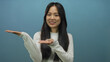 © Krakenimages.com - Woman extending hands presenting against blue background suggesting display or introduction, isolated and engaging young chinese female in casual attire.
