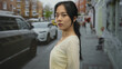 © Krakenimages.com - Young woman with black hair stands outdoors on a bustling urban street, surrounded by vehicles and buildings, capturing the essence of city life.
