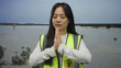 © Krakenimages.com - Young woman in reflective vest stands on a seaside beach in prayerful contemplation, embodying volunteering, mindfulness, and tranquility against a serene ocean backdrop.