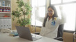 © Krakenimages.com - Young chinese woman doctor in a clinic uses a laptop at her desk, stethoscope around neck, surrounded by medical files and equipment in a bright, modern hospital room.