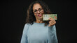 © Krakenimages.com - Middle-aged woman holding argentine banknotes against a black background, showcasing currency prominently in a studio-like setting.