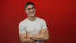 © Krakenimages.com - Young hispanic man with arms crossed wearing glasses and a white tee in a red studio; confidence approachability ease.