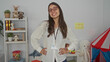 © Krakenimages.com - Teacher standing confidently in a kindergarten classroom with toys and educational materials, showcasing a young hispanic woman dedicated to preschool education indoors.