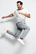 © SHOTPRIME STUDIO - Energetic young smiling man in white t-shirt jumps joyfully against a light gray background, showcasing a fun and lively lifestyle. Active movement concept.