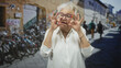 © Krakenimages.com - Woman shows ok sign with hands and colorful glasses on a city street lined with parked bicycles and old buildings; joyful independence.