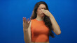 © Krakenimages.com - Hispanic teenager woman pinches nose in blue studio setting with visible hand gesture and wrinkled nostril; disgust aversion odor.