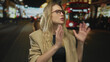 © Krakenimages.com - Woman outdoors at night in city wearing glasses and brown coat standing on busy street with red bus and lights behind, expressing surprise or discussion in urban setting.