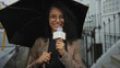 © Krakenimages.com - Young woman reporter with curly hair holding microphone and umbrella on a rainy street outdoors delivering news report