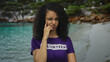 © Krakenimages.com - Young woman with curly hair stands on a beach wearing a purple volunteer shirt, showcasing a thoughtful expression against a serene seaside backdrop.