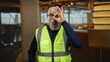 © Krakenimages.com - Middle-aged man in reflective safety vest making an okay gesture in a modern indoor hotel environment with amused expression and warm lighting.