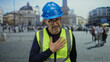 © Krakenimages.com - Elderly man wearing safety vest and helmet stands in saint peter's square at vatican city, hand on chest, expressing gratitude amidst a bustling cityscape backdrop.