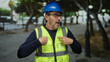 © Krakenimages.com - Man wearing safety gear points to himself in urban park, featuring high-visibility vest and blue helmet in an outdoor city environment.