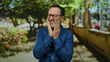 © Krakenimages.com - Man in a blue shirt with glasses outdoors in a park expressing discomfort or pain against a blurred natural background