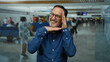 © Krakenimages.com - Man smiling in airport terminal with blurred background, wearing blue shirt, making hand gesture, mature age, reflecting happiness, in an indoor public space.