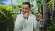 © Krakenimages.com - Hispanic man in white coat holding dental aligner outdoors in park setting, pointing with expression of guidance and professionalism among lush greenery.