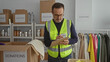 © Krakenimages.com - Mature man in charity center organizing donation boxes and taking notes while wearing a reflective vest surrounded by clothing and supplies.