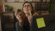 © Krakenimages.com - Woman with glasses crossing fingers in an office setting, expressing hope or anticipation, sitting at a desk with shelves and books in the background.