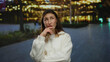 © Krakenimages.com - Woman contemplating thoughtfully in an outdoor city street setting with blurred illuminated lights, wearing white outfit, creating a serene urban night ambiance.