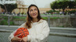 © Krakenimages.com - Young woman in white sweatshirt holding basketball with happy expression outdoors on a city street, surrounded by urban landscape and trees, enjoying a leisurely day.