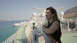 © Krakenimages.com - Woman leaning on rail on cruise deck building, smiling with sunglasses on head, hands folded on railing while looking toward sea and horizon; vacation relaxation.