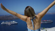 © Krakenimages.com - Woman with bare back raising arms at santorini building viewpoint overlooking caldera and cruise ships; travel memories serenity.
