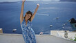 © Krakenimages.com - Woman smiling with arms out on building terrace overlooking sea and boats in santorini town; vacation relaxation joy.