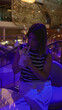 © Krakenimages.com - Young hispanic brunette woman sipping a cocktail at a bar under blue disco lights while seated and stirring with a straw; relaxed evening.